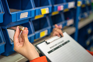 A hand holds a part and clipboard with instructions.